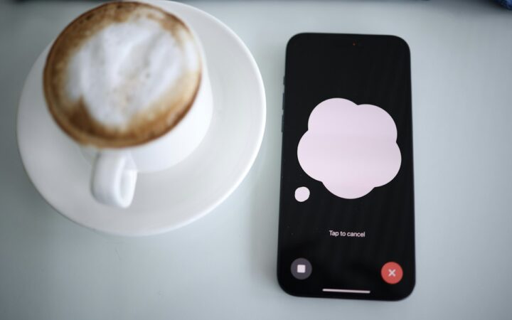 A smartphone displaying the ChatGPT voice interface beside a cup of coffee, photographed by Solen Feyissa in 2024