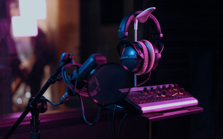 Microphone, studio headphones and an audio mixer under blue and purple lighting, illustrating recorded-audio transcription