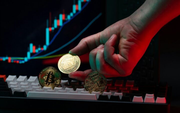 A hand holds an Ethereum-themed coin above a keyboard, with a trading chart in the background
